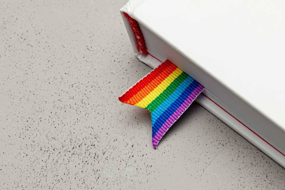 Image of a book with a rainbow book marker to communicate a need for more LGBTQ focused education. Featured in the Origins of Pride blog.
