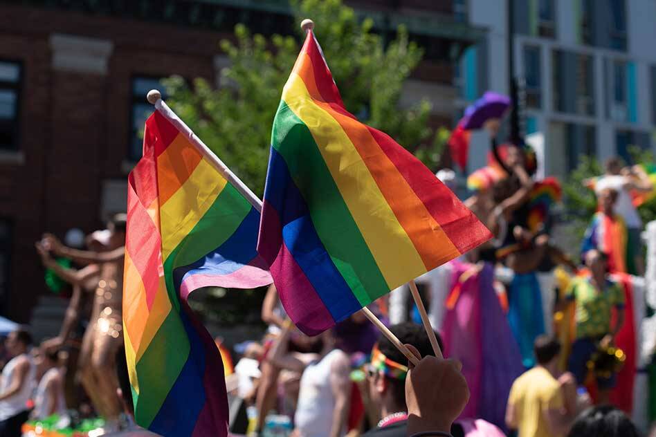 Image depicting flags flying at a Pride March with copy overlaid to communicate a need to understand the reason behind the purpose of the march: Inform, Engage, Educate. Featured in the Origins of Pride blog.