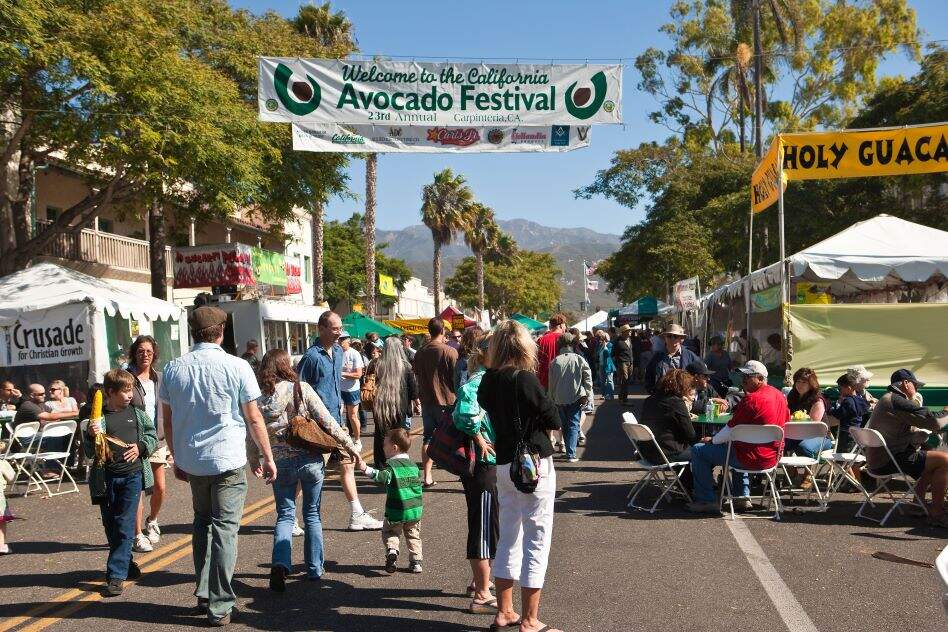 People and stalls with signs for a big avocado festival taking place in California.